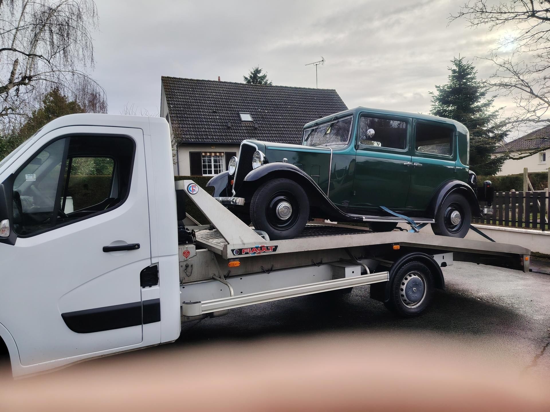 Voiture ancienne verte sur une dépanneuse blanche à plateau. Extérieur, ciel couvert.