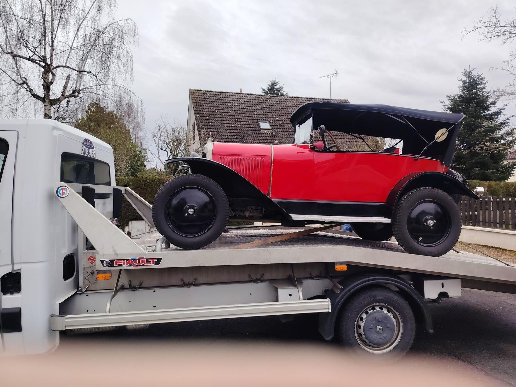 Voiture ancienne rouge sur une dépanneuse à plateau. Jantes, capote et extérieur noirs.
