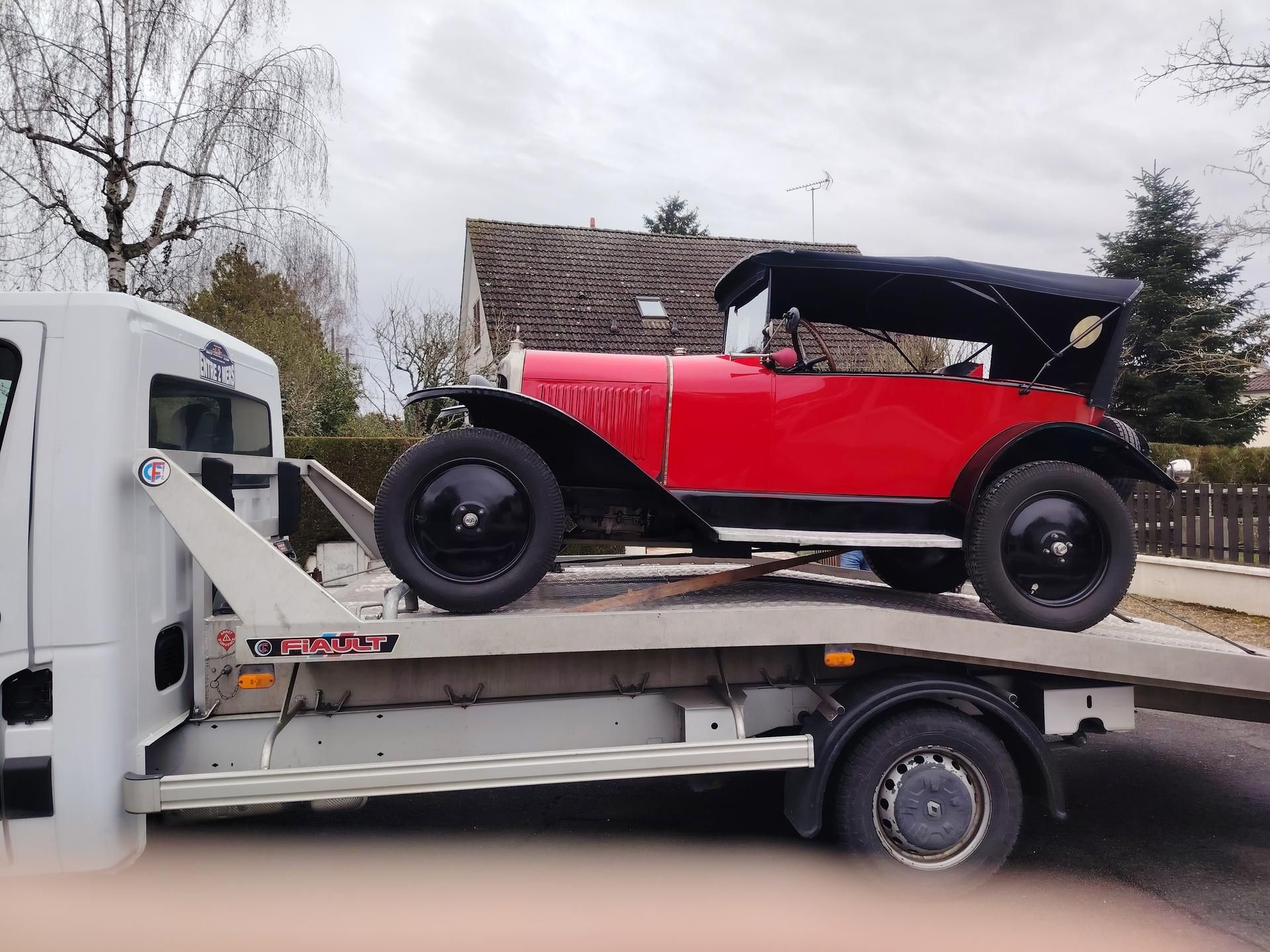 Voiture ancienne rouge sur une dépanneuse à plateau. Jantes, capote et extérieur noirs.