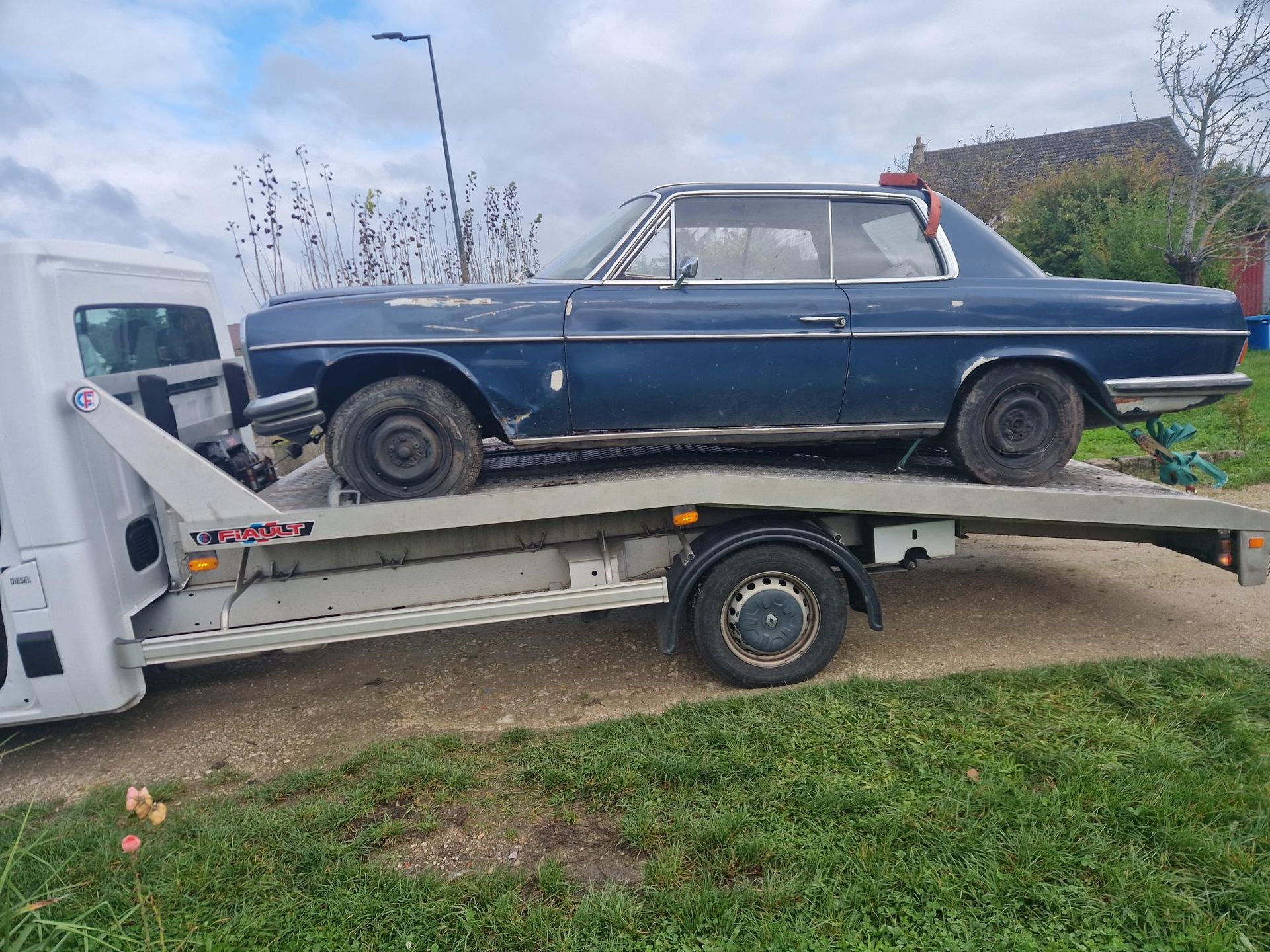 Une voiture ancienne bleue chargée à l'extérieur sur une dépanneuse blanche à plateau.