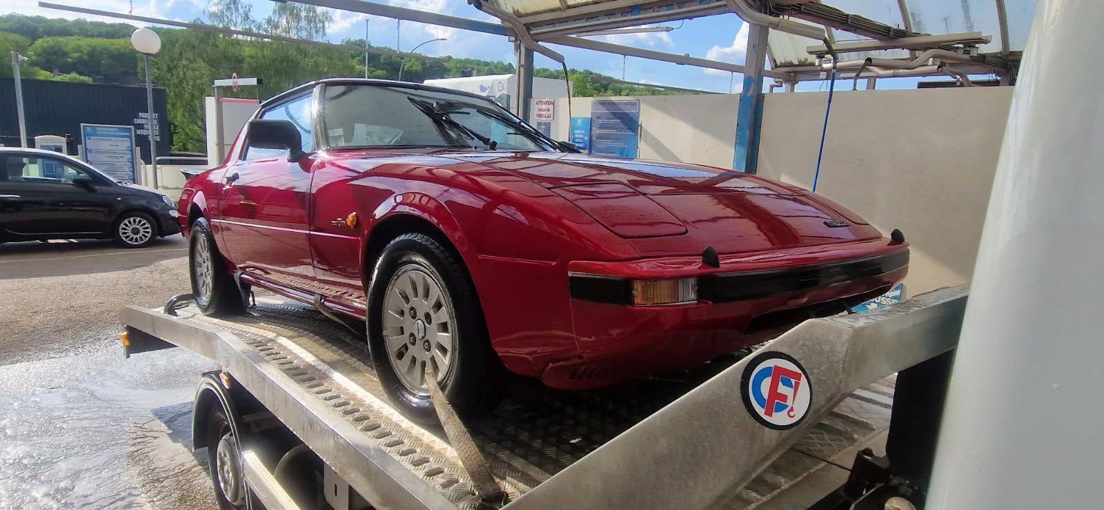 Voiture de sport rouge sur une plateforme de lavage auto sous un auvent.