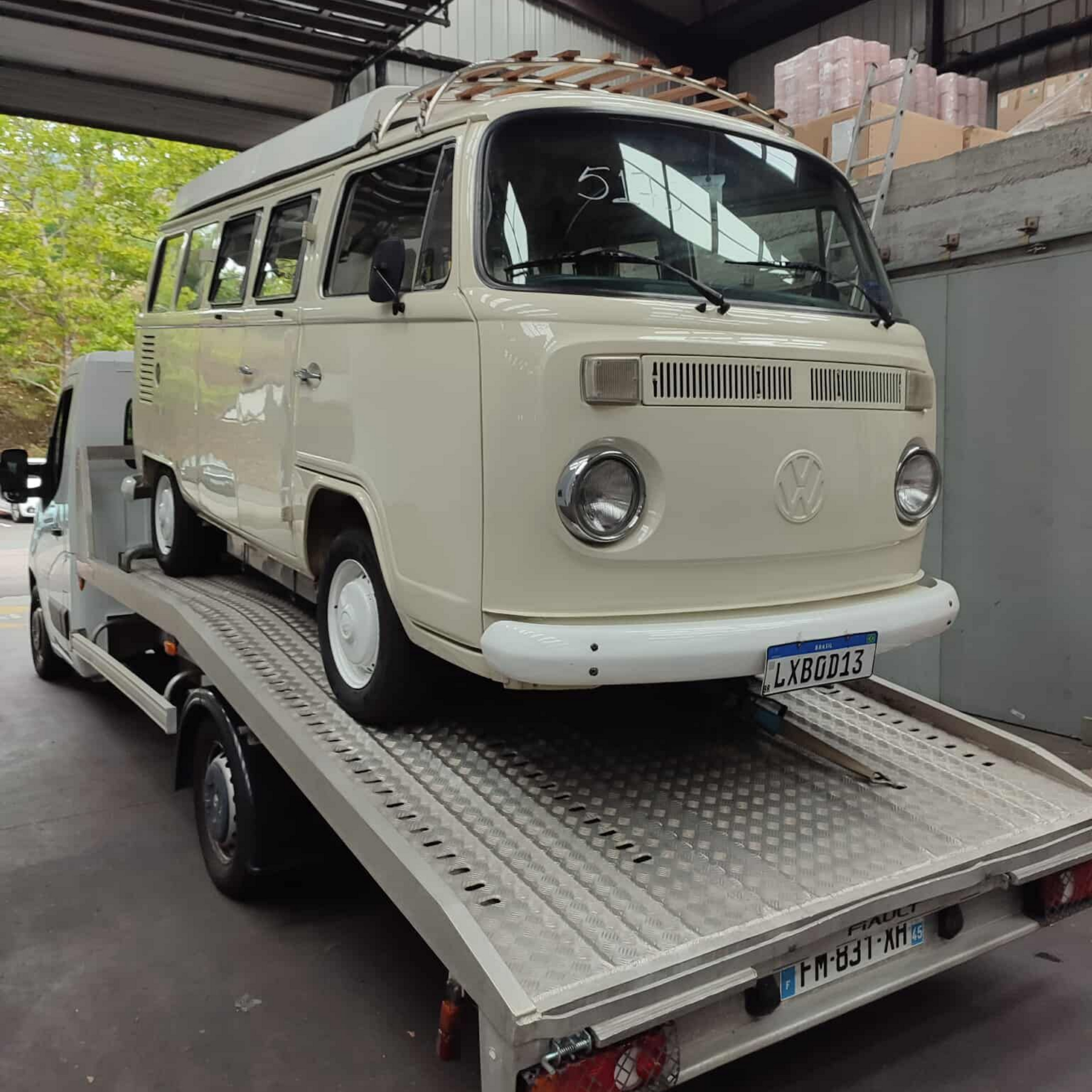 Un combi Volkswagen vintage couleur crème sur une dépanneuse à plateau. À l'intérieur d'un garage.