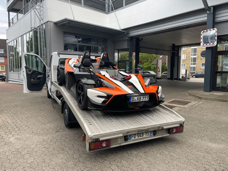 Véhicule à quatre roues orange et blanc sur une dépanneuse ; stationné devant un bâtiment.