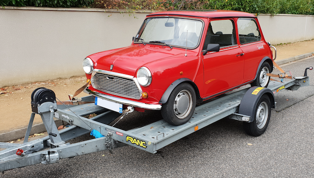 Une MINI Cooper classique rouge sur une remorque grise, garée dans une rue.