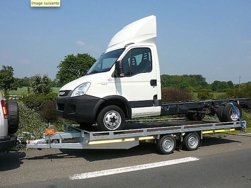 Camion blanc à châssis-cabine sur une remorque, stationné sur une route. Ciel dégagé, en journée.