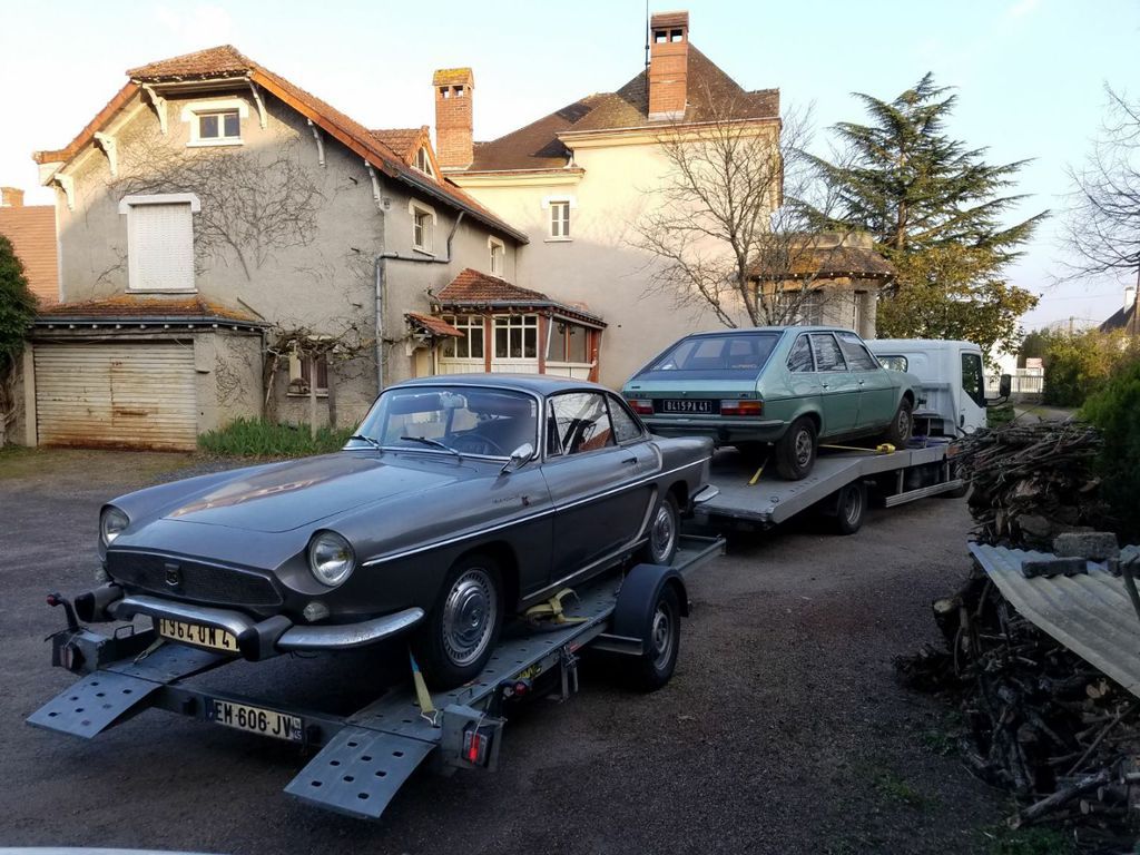 Trois voitures anciennes sur des remorques devant un bâtiment en pierre.