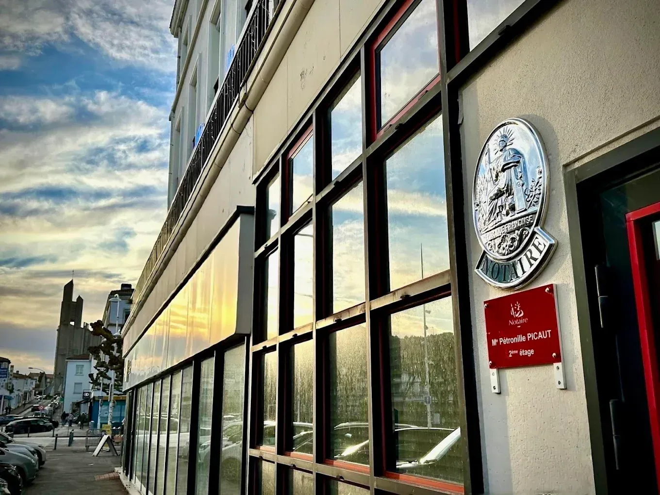 Un maillet en bois repose sur un bureau devant un professionnel tenant un livre et rédigeant un document.