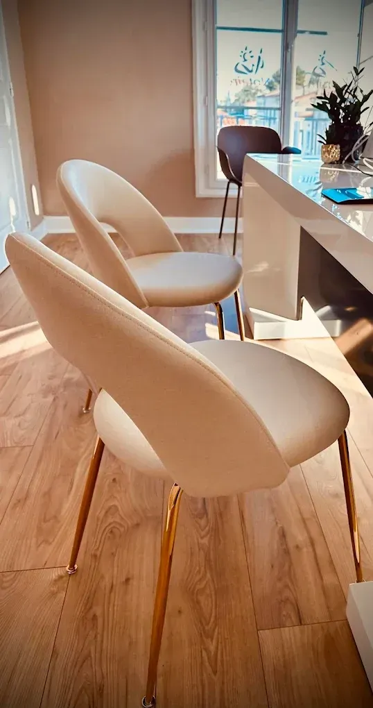 Deux chaises aux pieds dorés sont placées sur un parquet clair près d'un bureau moderne.