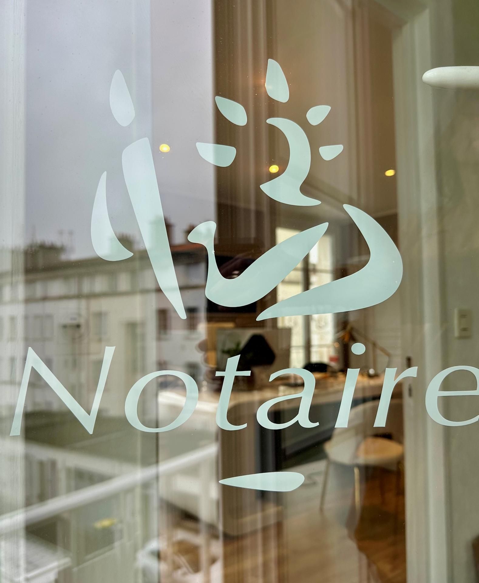Autocollant dépoli sur une porte vitrée représentant un logo stylisé au-dessus du mot Notaire, avec un bureau visible en arrière-plan.