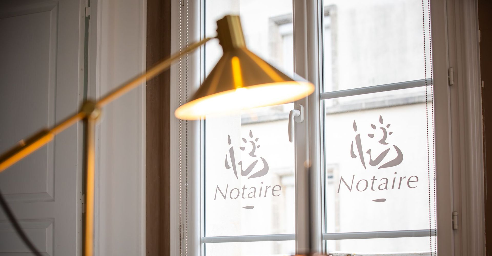 Vue en contre-plongée d'un immeuble à plusieurs étages avec une façade claire, une devanture commerciale au rez-de-chaussée et un balcon métallique.