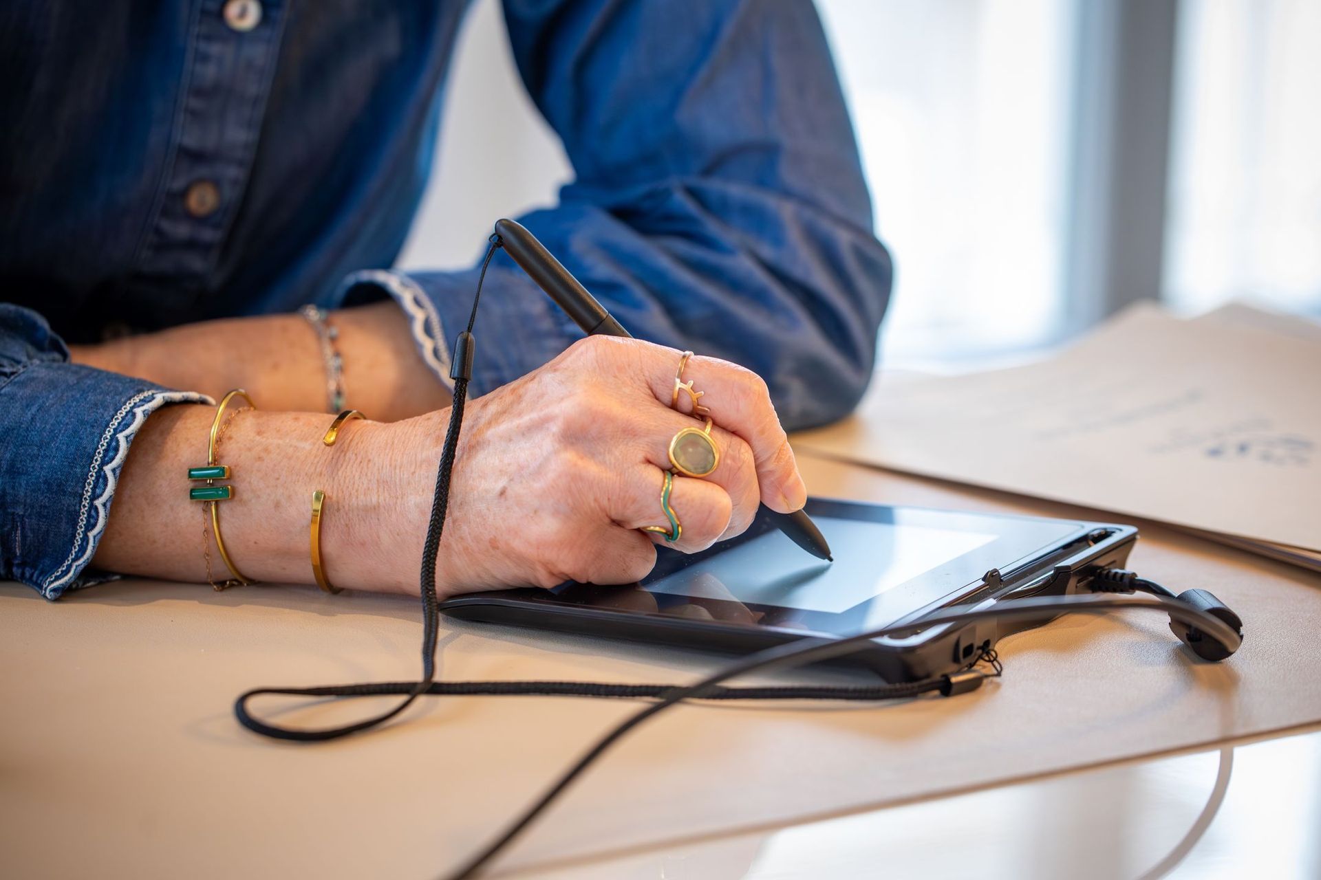 Une personne portant une montre tient un stylo-plume au-dessus d'un document vierge posé sur une table en bois.