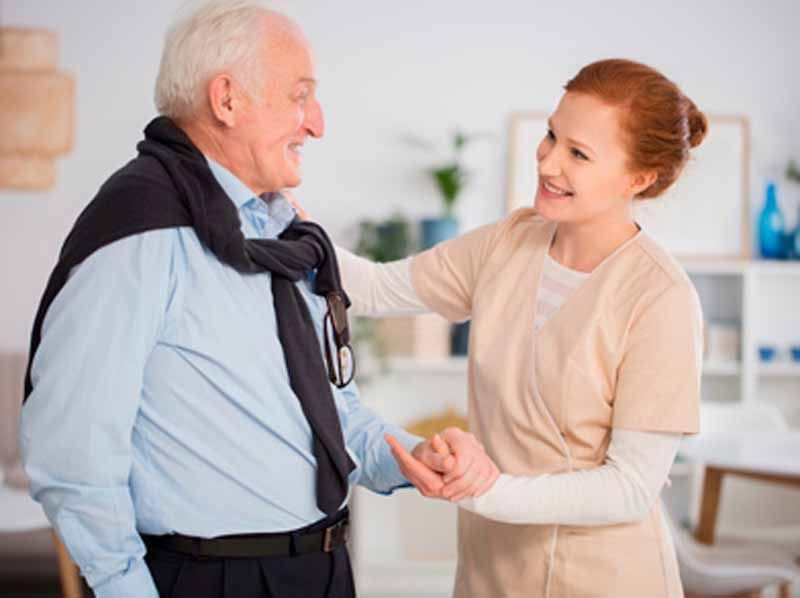 Una enfermera sostiene la mano de un anciano en una sala de estar.