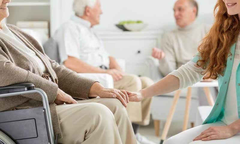 Una mujer sostiene la mano de una anciana en silla de ruedas.