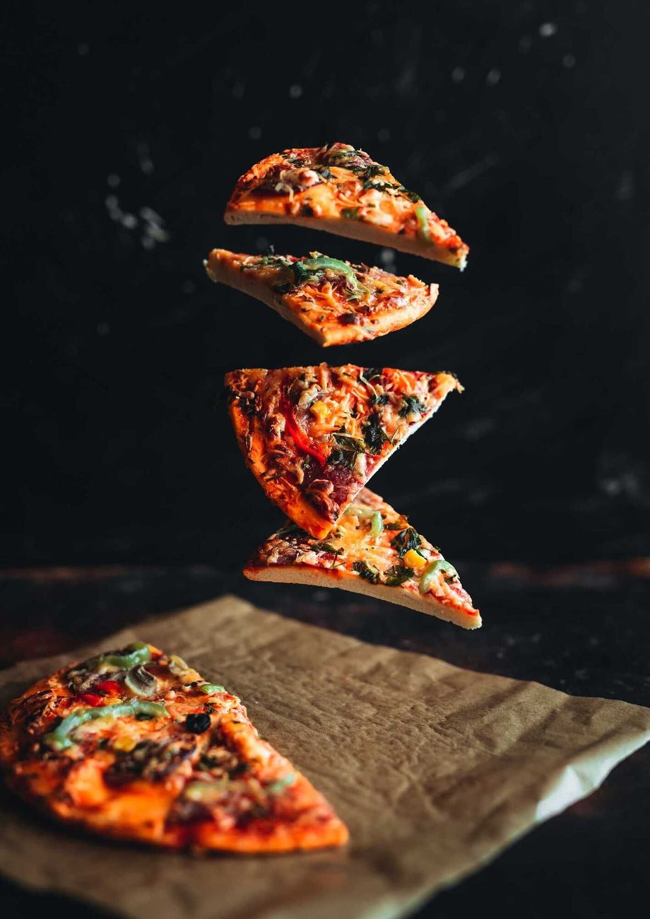 Des parts de pizza flottant au-dessus d'une surface recouverte de papier sulfurisé sur fond sombre.
