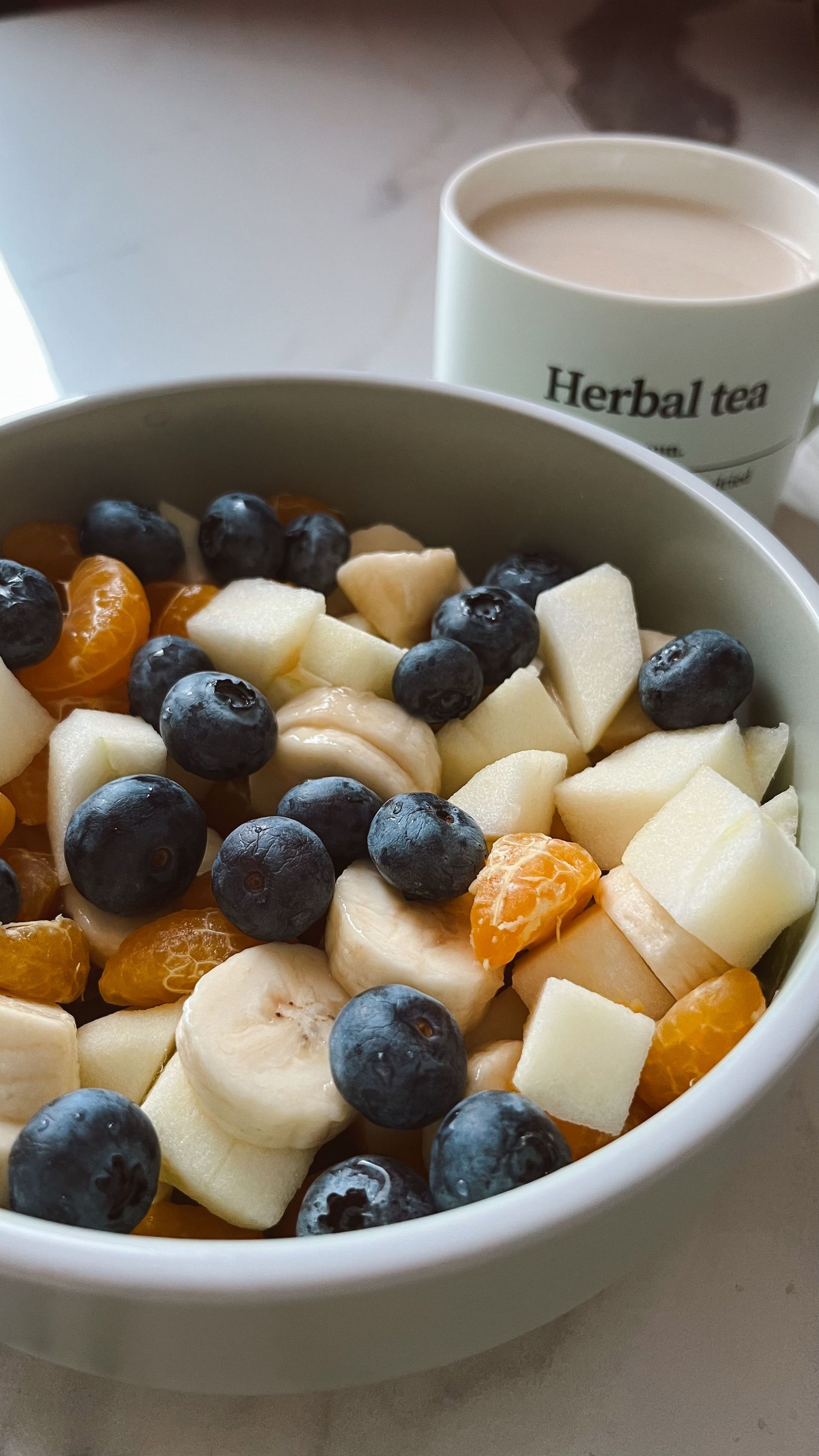 Bol de fruits mélangés avec des myrtilles, de l'ananas et des bananes, accompagné d'une tasse de tisane