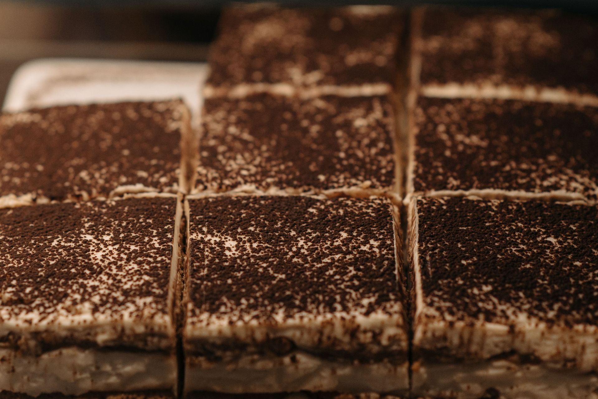 Des rangées de carrés de gâteau au chocolat saupoudrés de cacao en poudre sur un plateau