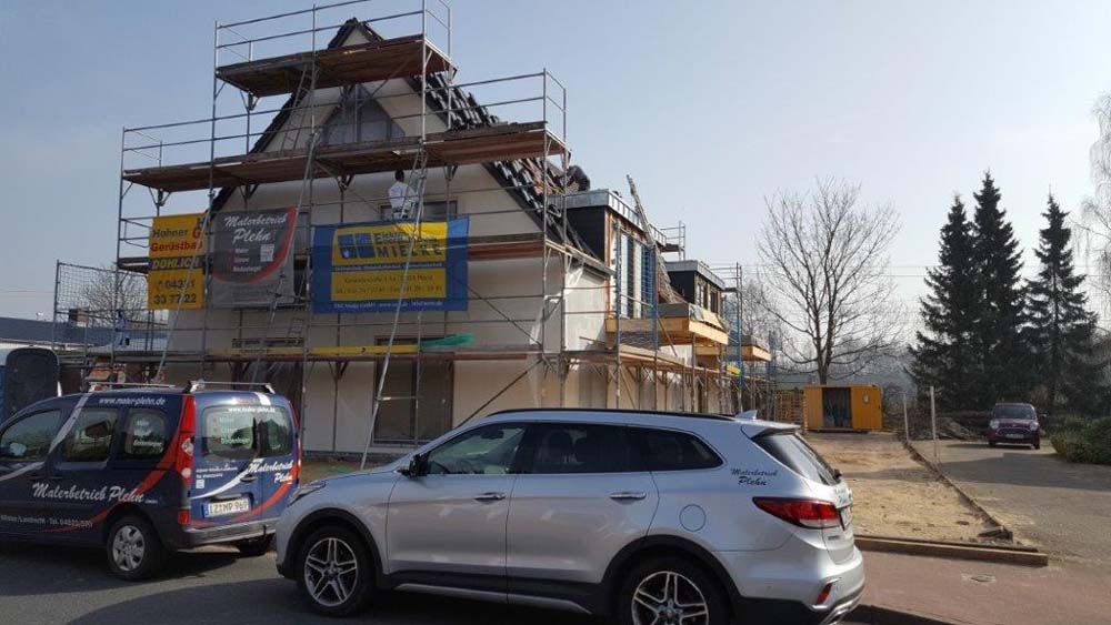 Gebäude im Bau mit Gerüst; roter Backstein, weiße Zierleisten und braunes Dach.