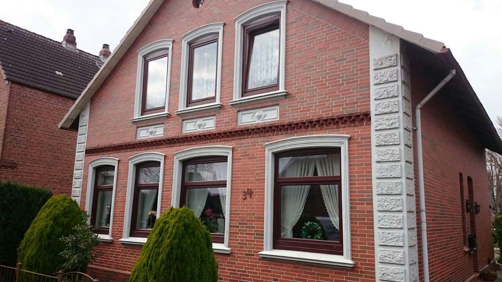 A-förmiges Haus mit Glasfront, gelben Zierleisten, Balkon und Grünflächen.