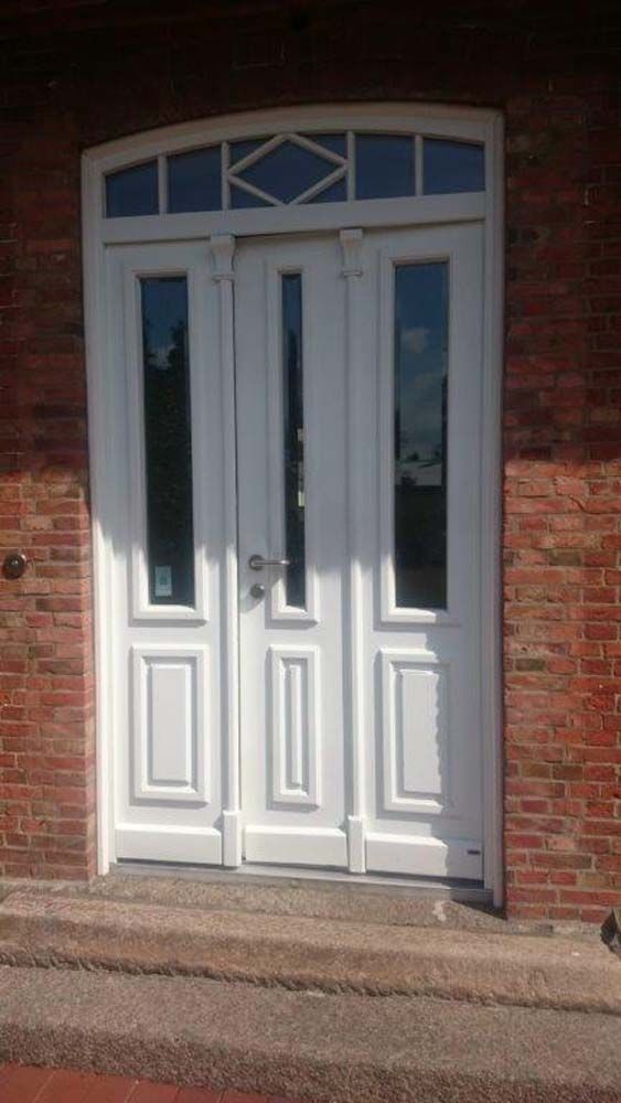 Weiße Doppeltüren mit Glaseinsätzen und gewölbtem Oberlicht, in einem Backsteingebäude eingebaut.