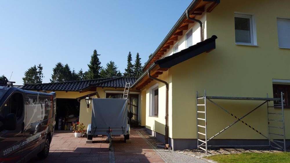 Gelbes Haus mit dunklem Dach und Dachrinne, Baustelle.