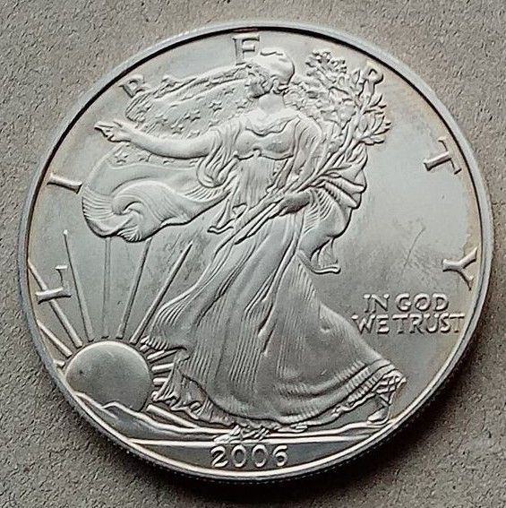Silbermünze mit dem Bildnis der Freiheitsstatue, die einen Zweig hält, im Hintergrund geht die Sonne auf. „IN GOD WE TRUST“ „2006“.