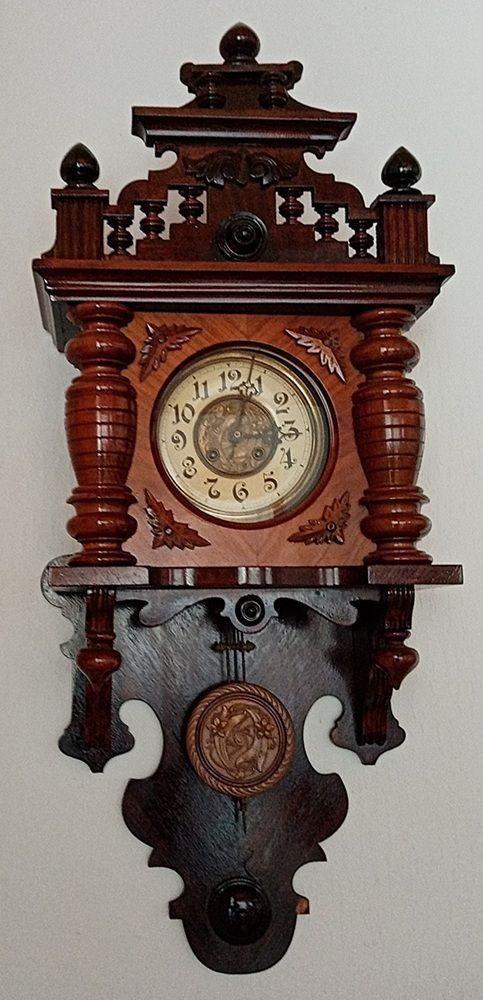 Antike hölzerne Wanduhr mit kunstvollen Schnitzereien, Pendel und Zifferblatt.