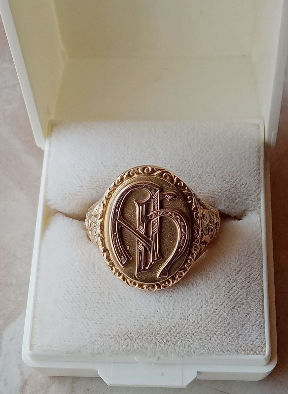 Goldring mit ineinander verschlungenen Initialen in einer dekorativen Fassung, präsentiert in einer kleinen Schachtel.