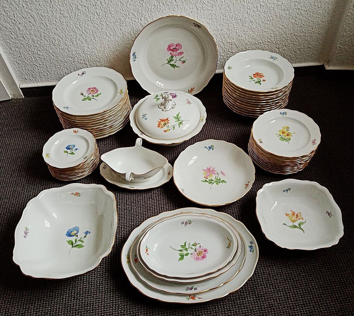 Weißes Porzellangeschirr mit floralen Mustern und Goldrand.