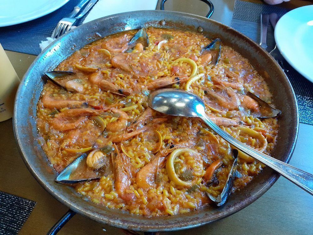 Paella con camarones, mejillones y calamares en una sartén grande con una cuchara para servir.