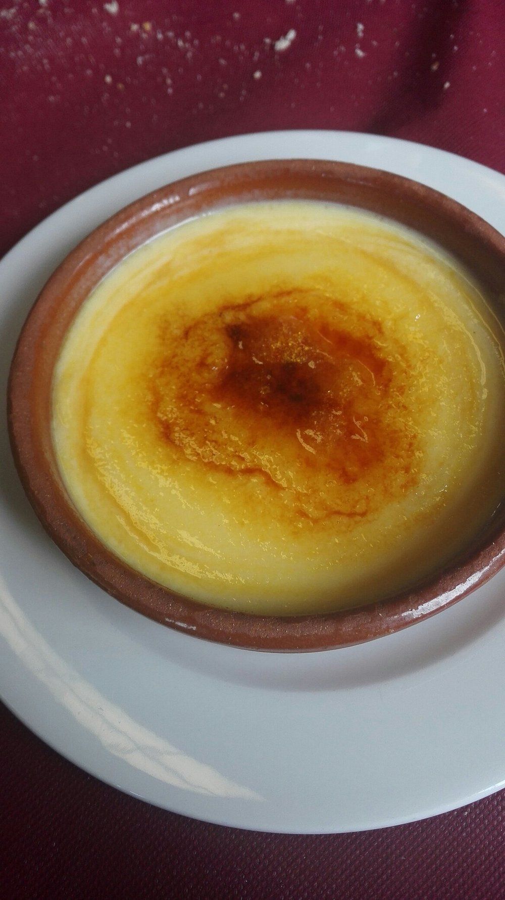Crème brûlée en un ramequín de cerámica marrón sobre un plato blanco; cobertura de azúcar caramelizado.
