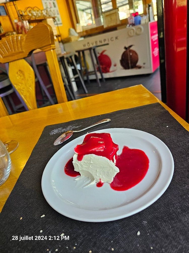 Postre en plato blanco: merengue con salsa de frambuesa. Cuchara, mesa amarilla, ambiente de restaurante.