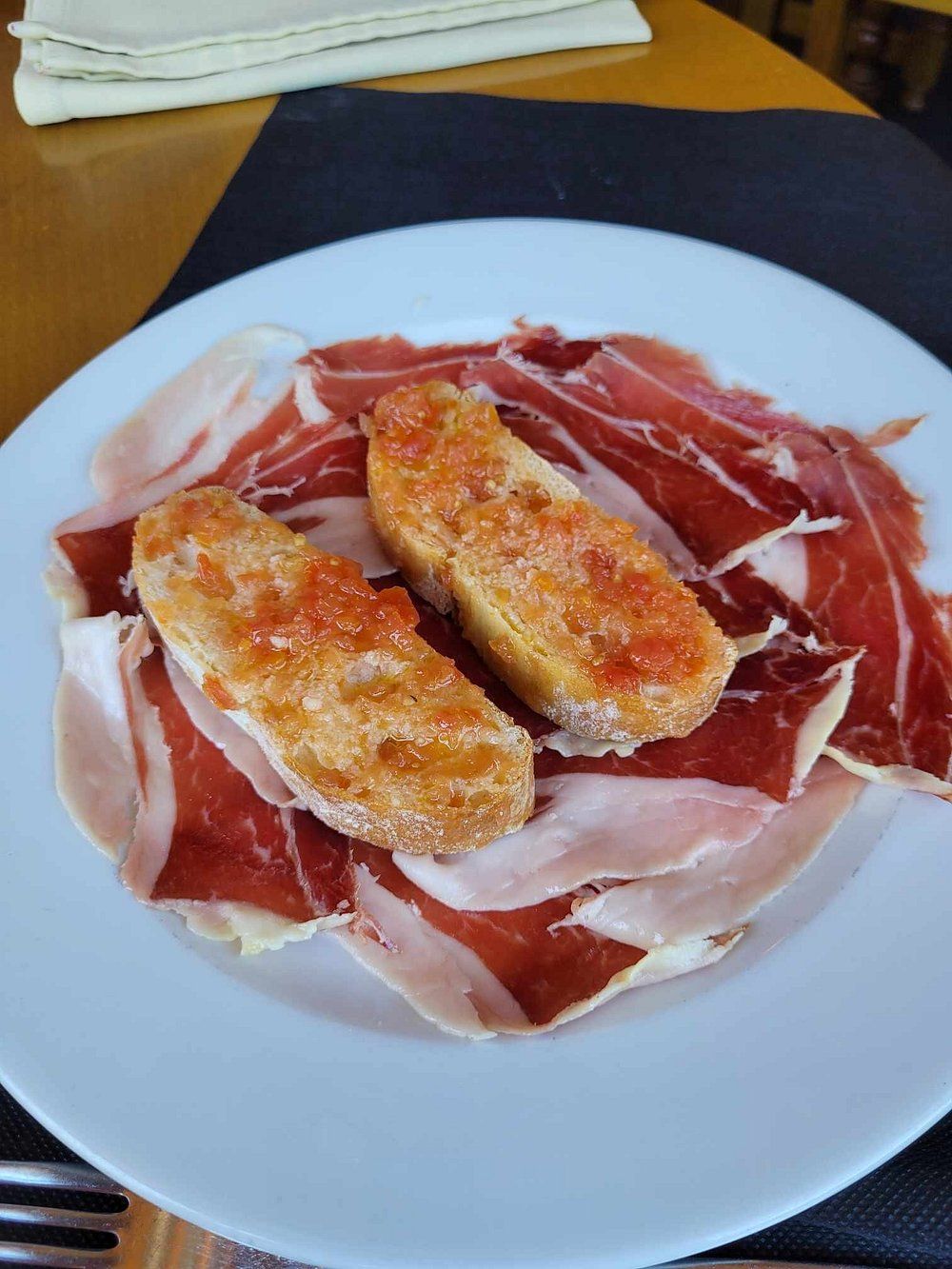 Plato de jamón serrano y dos rebanadas de pan tostado con tomate.