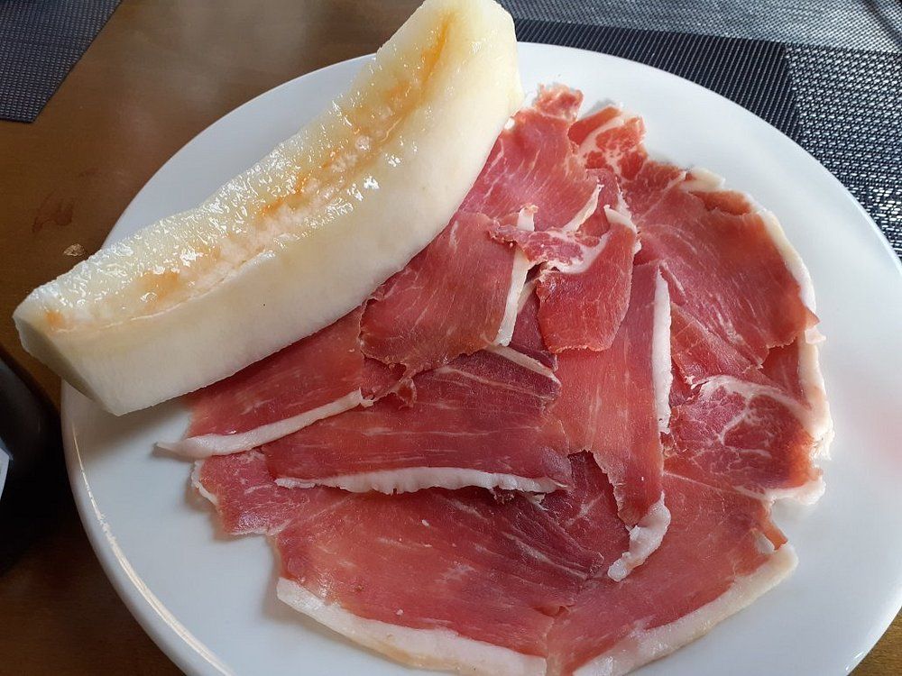 Jamón y melón cortados en rodajas en un plato blanco.