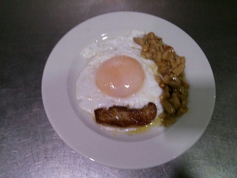 Huevo frito con guarnición de verduras cocidas y una rodaja de carne en un plato blanco.