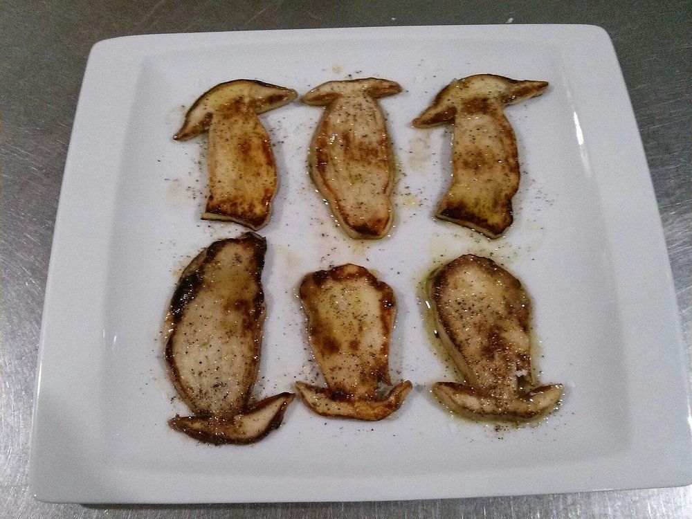 Seis rodajas de hongo ostra salteadas en un plato rectangular blanco.