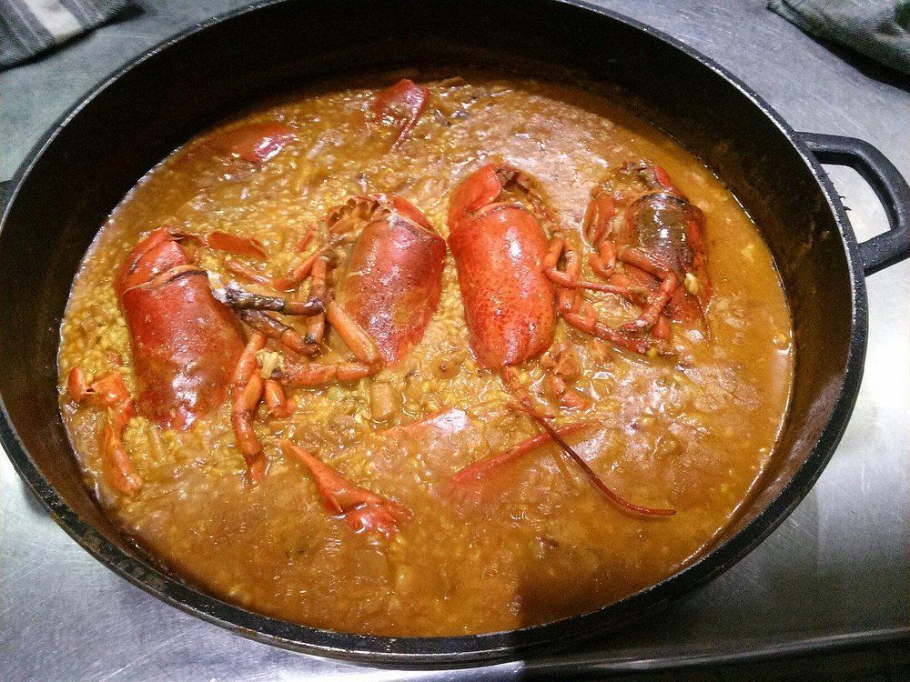 Plato de langosta y arroz en olla negra; las langostas rojas reposan sobre el arroz amarillo-marrón.