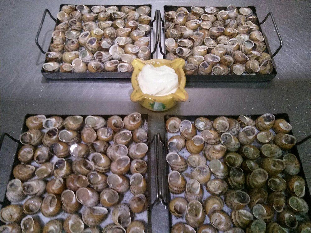 Cuatro bandejas de caracoles con mantequilla en una fuente, listas para servir.