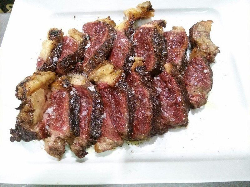 Filete de ternera a la parrilla cortado en rodajas, a punto medio, sobre un plato rectangular blanco.