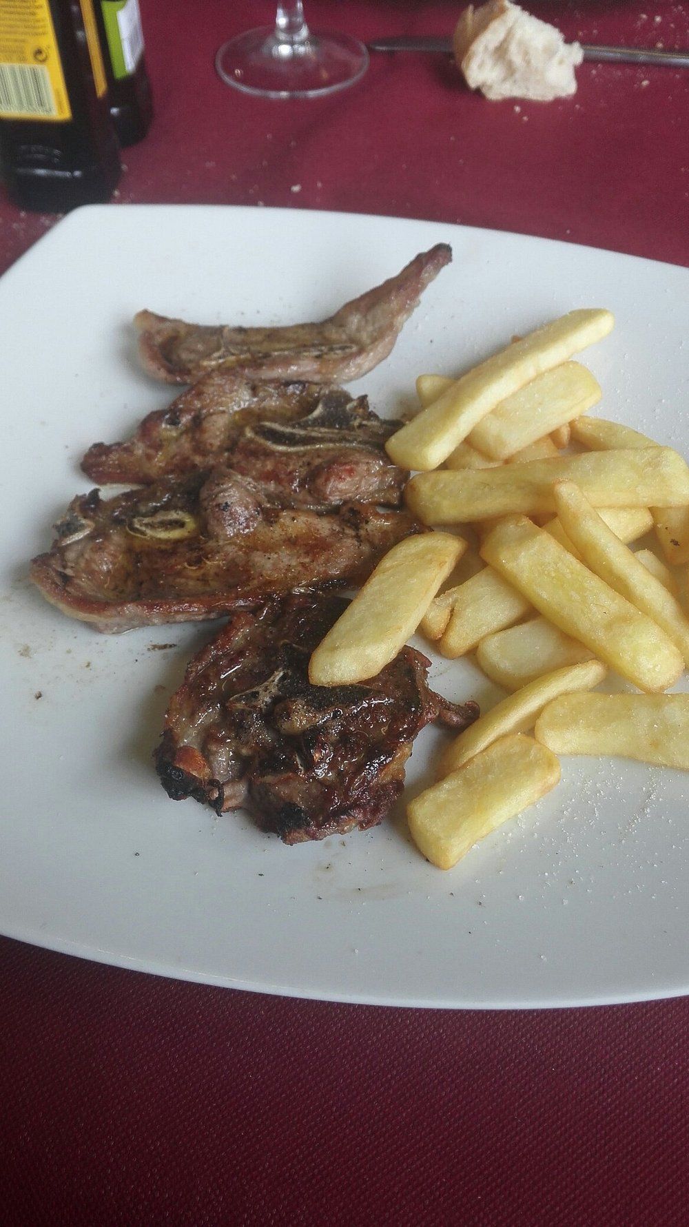 Chuletas de cordero a la parrilla con patatas fritas en un plato blanco.