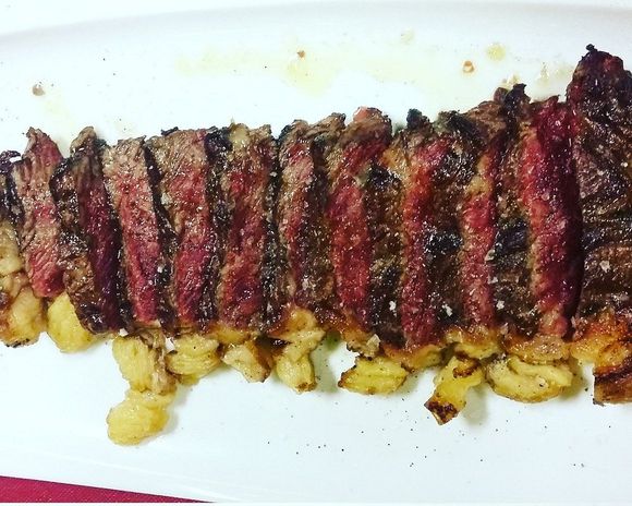 Filete cortado en rodajas sobre una cama de patatas asadas, presentado en un plato blanco.