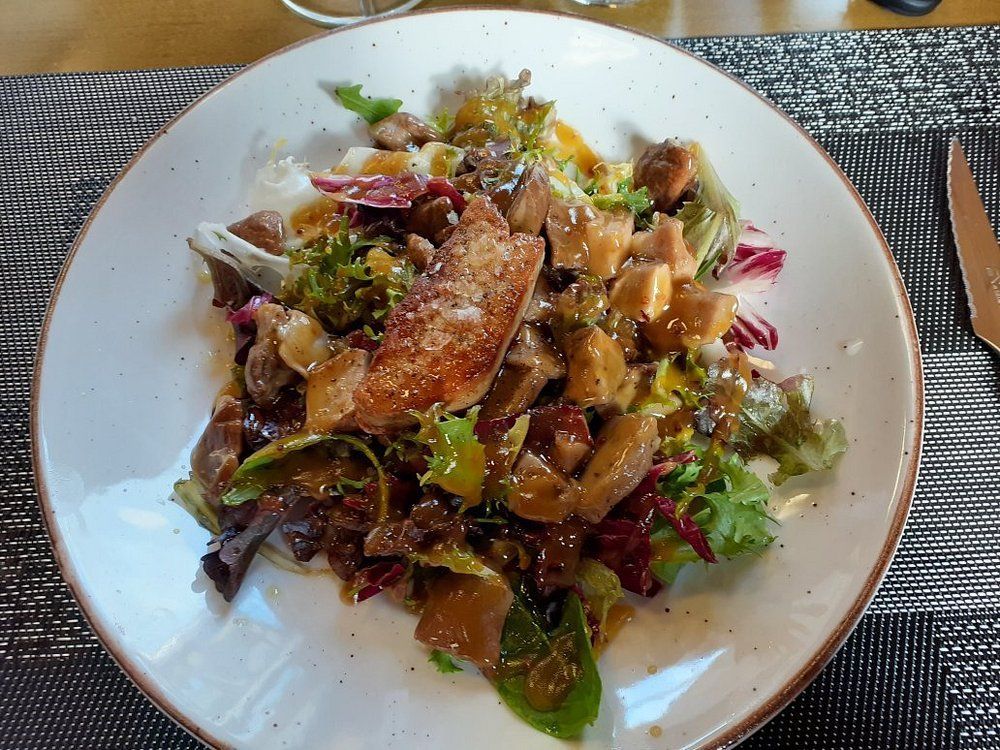 Ensalada con verduras, champiñones y cobertura dorada en un plato blanco.