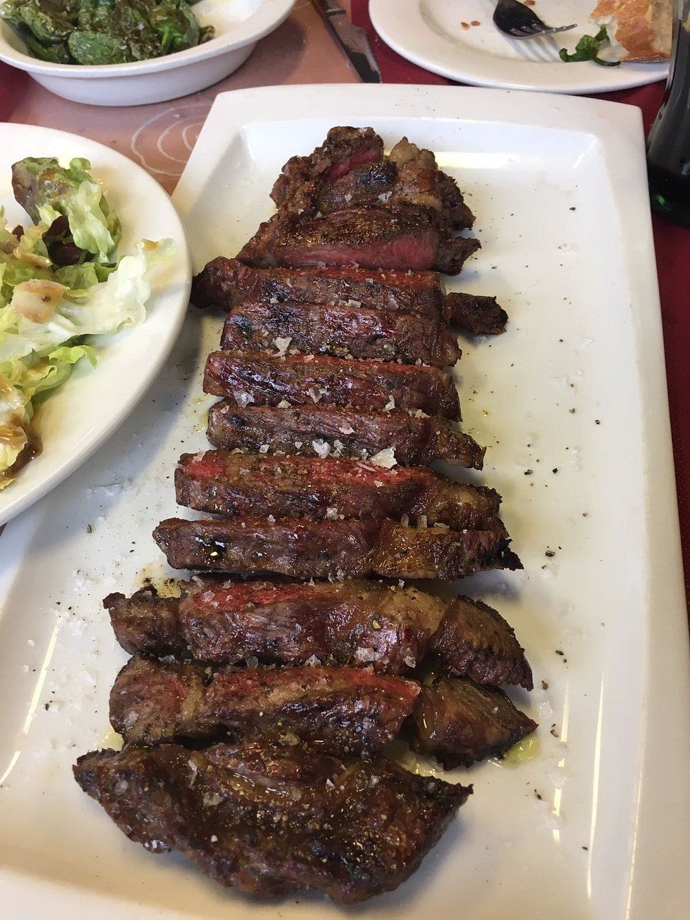 Filete cortado en rodajas en un plato blanco, junto a ensalada y otro plato.