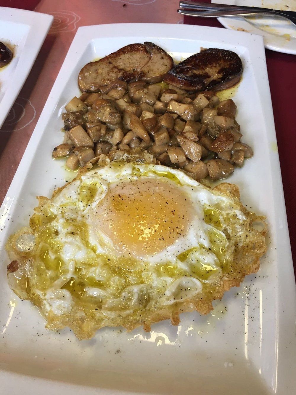 Plato de comida: huevo frito, champiñones salteados y carne con salsa.
