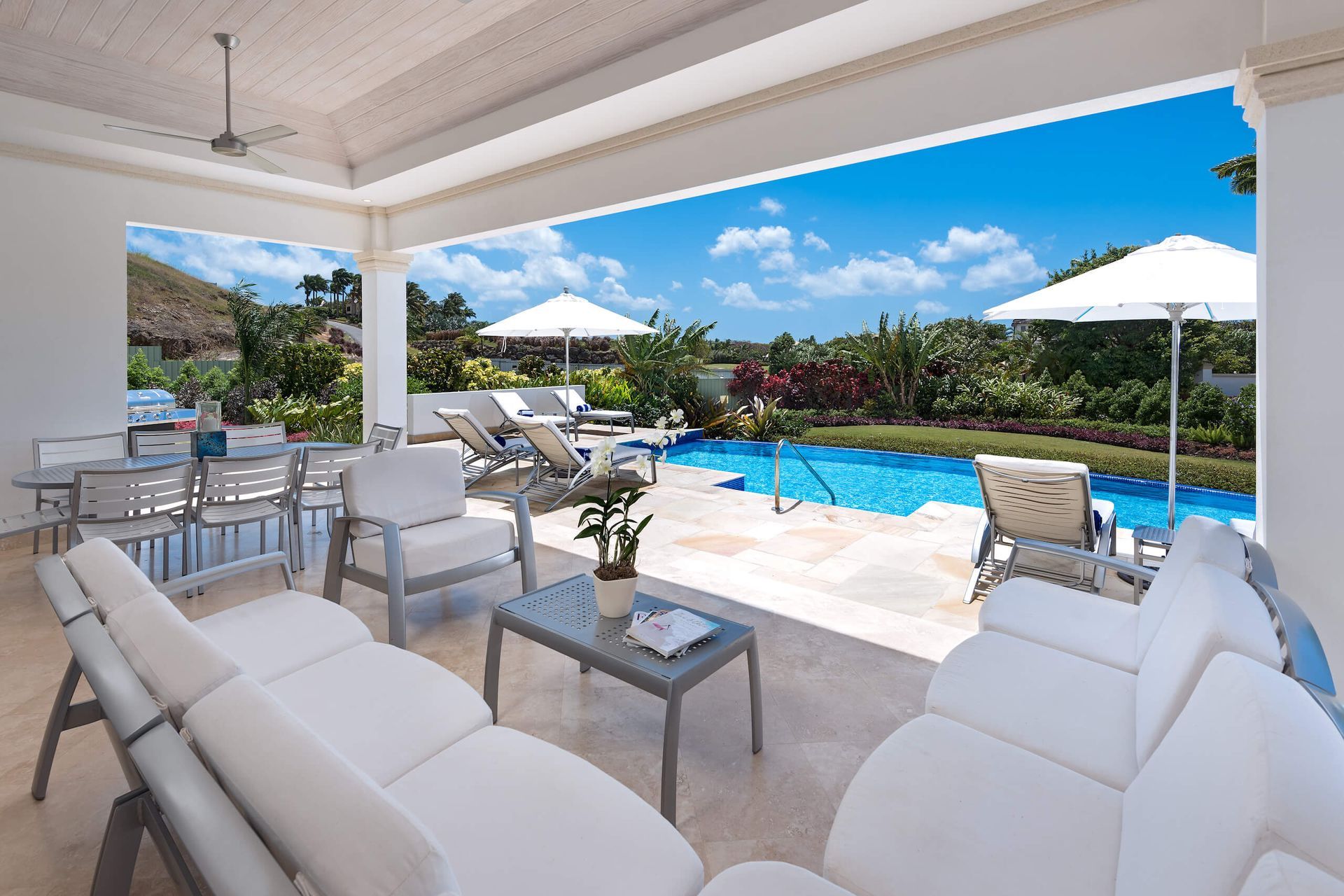 a patio with white furniture and umbrellas overlooking a swimming pool
