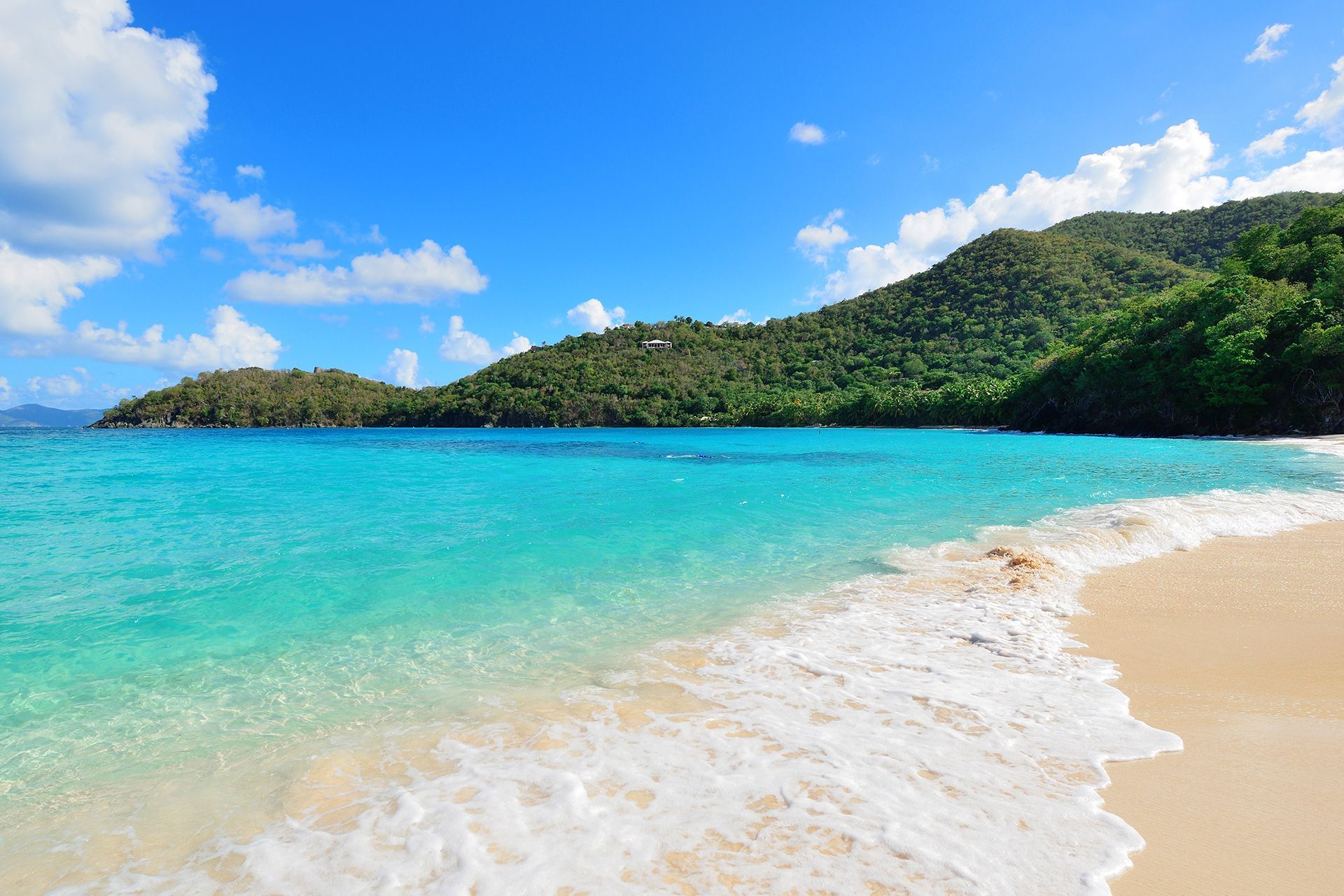 a sandy beach with turquoise water and mountains in the background .