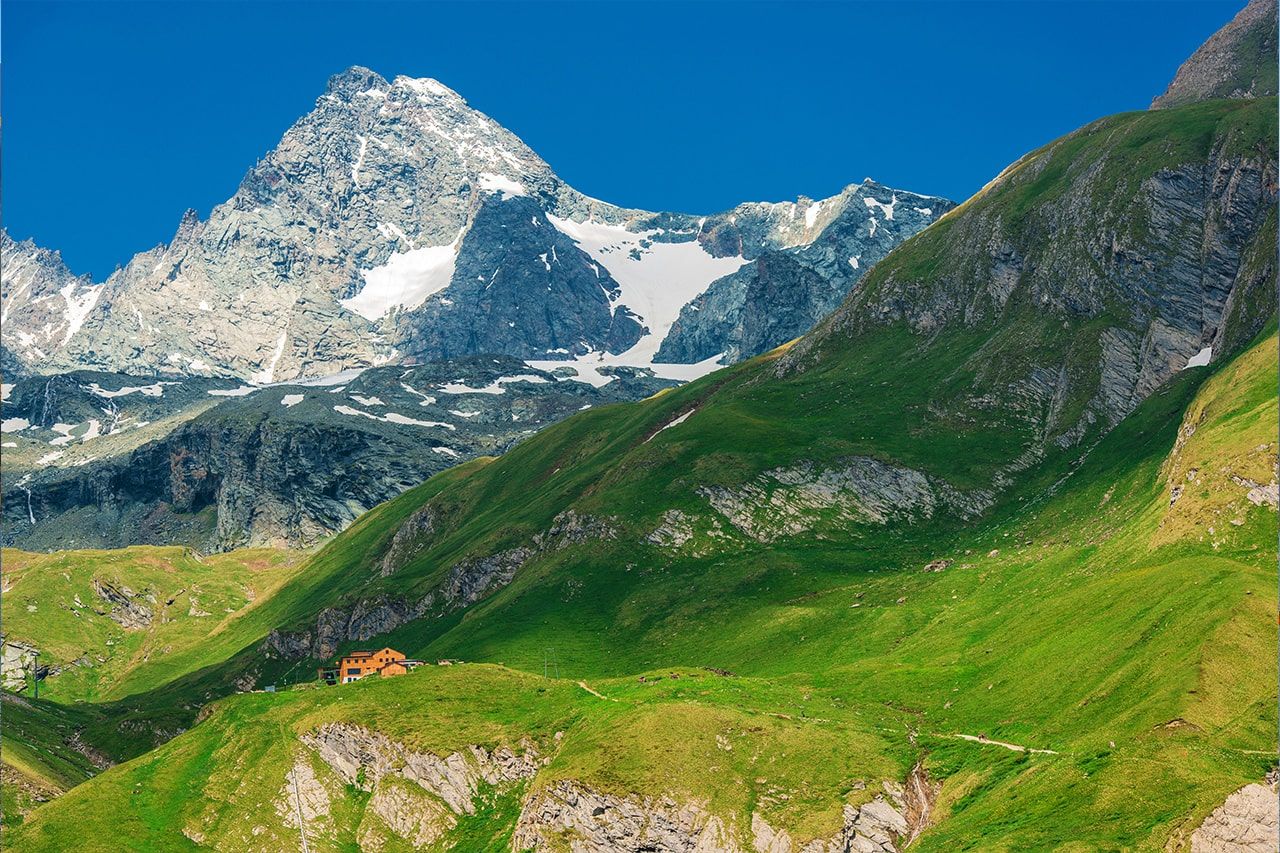 a mountain covered in snow and grass with a blue sky in the background