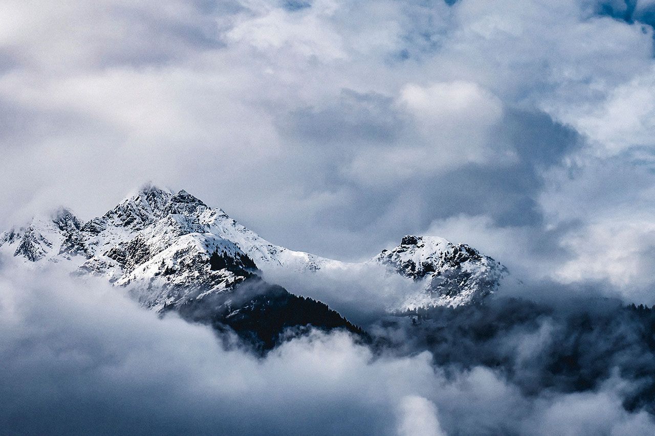 a mountain covered in snow is surrounded by clouds in the sky