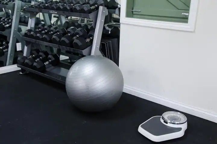 a gray exercise ball is sitting next to a scale in a gym .