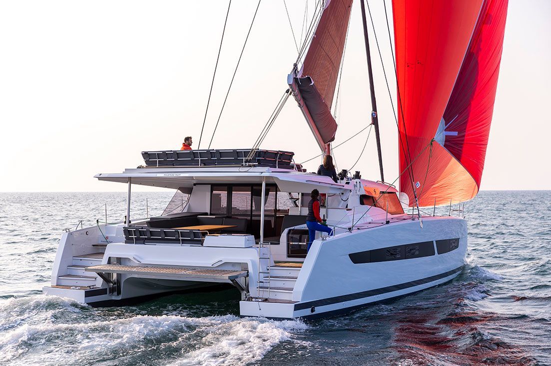 a white catamaran with red sails is floating on top of a body of water