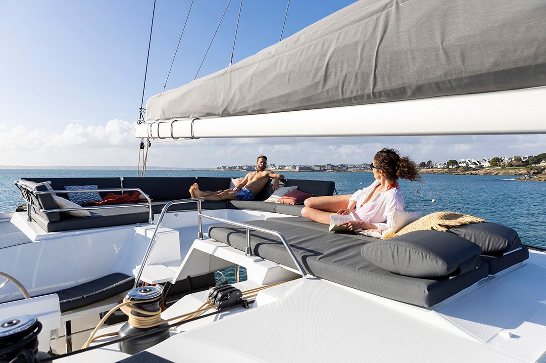a man and a woman are sitting on the deck of a sailboat in the ocean .